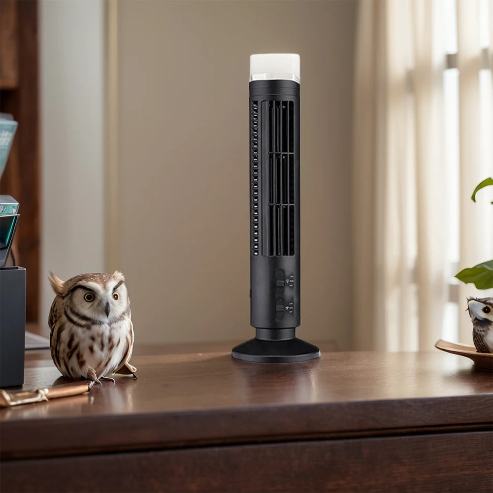 Black bladeless desktop tower fan placed on wooden desk near decorative owl figurines in a cozy room