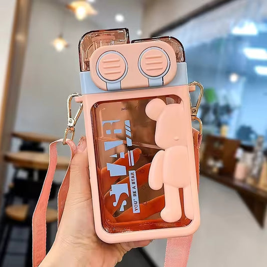 Pink cartoon bear water bottle with attached strap and decorative bear figure held indoors
