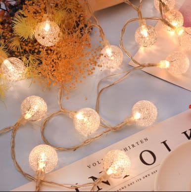 Warm white bubble ball LED string lights glowing softly near dried flowers on a table