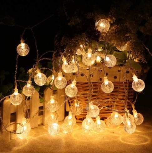 Clarify.pk bubble ball LED string lights glowing warmly with wicker basket and greenery in background