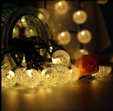 Warm glowing bubble ball LED string lights with textured clear globes near a mirror and a rose