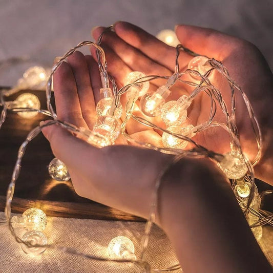 Hands holding glowing bubble ball LED string lights with warm white bulbs on dark surface