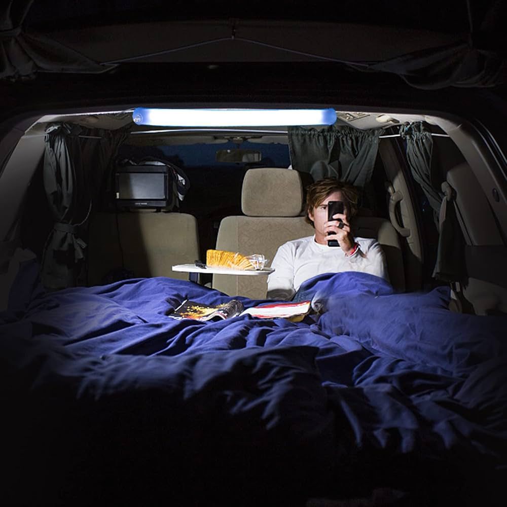 Camping inflatable light inside a car illuminating a person using a phone while lying on a bed with blue bedding