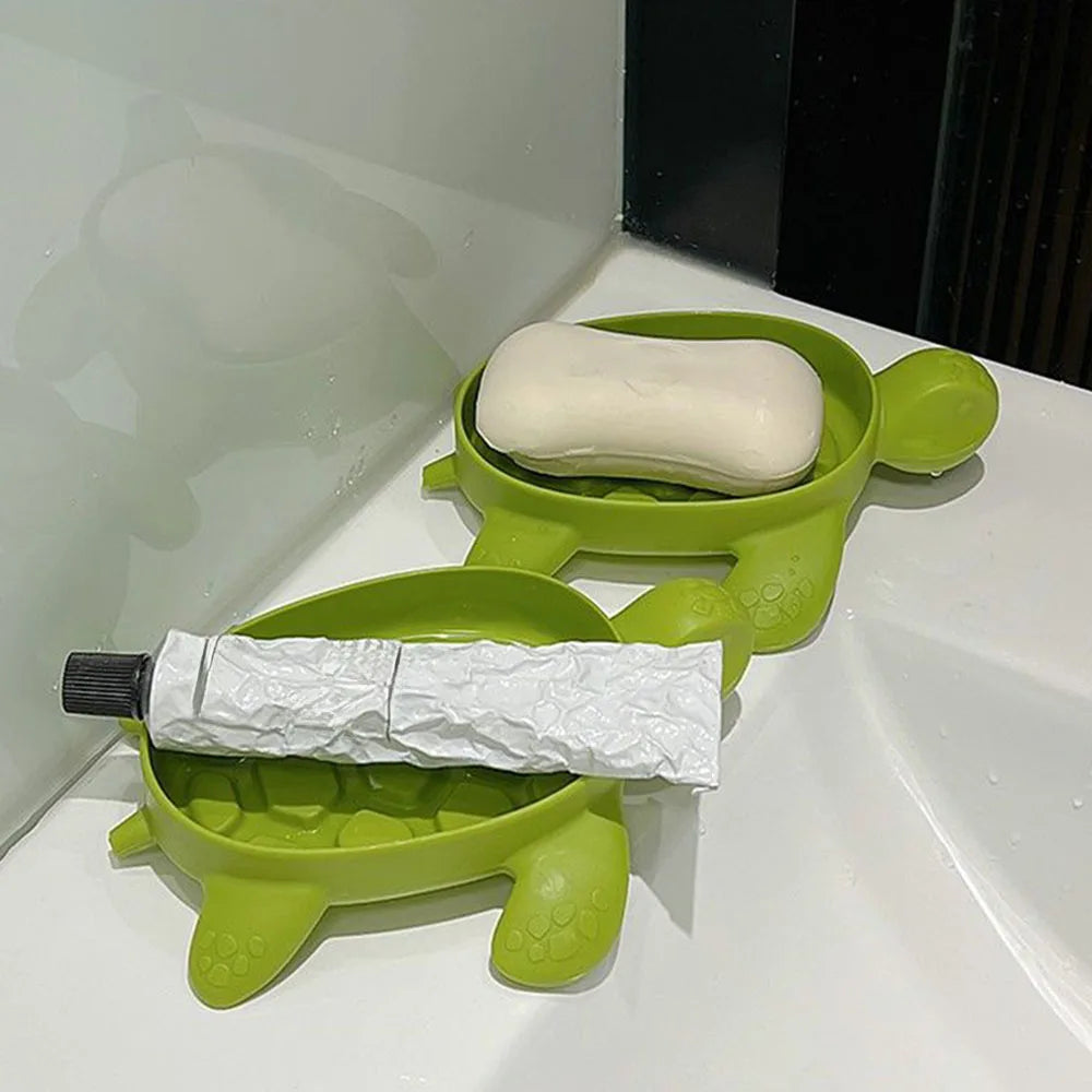 Green cartoon turtle soap holder with soap and toothpaste tube on a white sink surface