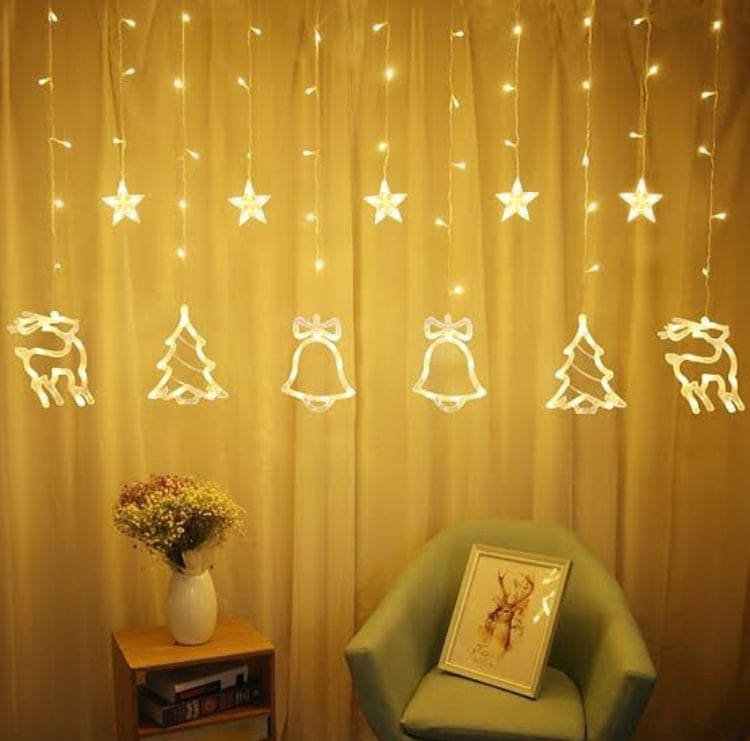 Warm yellow Christmas star fairy lights hanging with shapes of stars, bells, trees, and reindeer over a cozy room setup