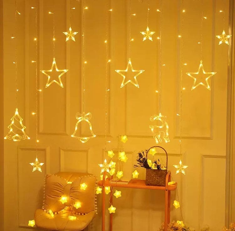Warm yellow Christmas star fairy lights hanging with star, bell, tree, and reindeer shapes decorating a cozy room