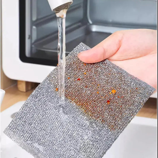 Hand holding metallic double sided scrubber pads being rinsed under faucet removing stuck on food bits