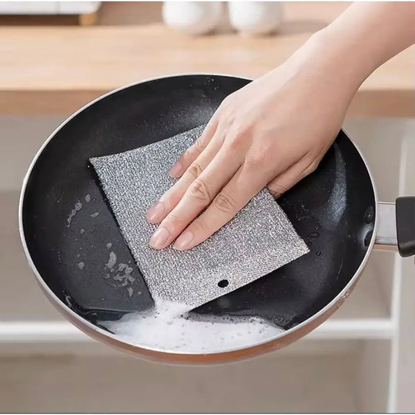 Hand using gray textured double sided scrubber pads to clean a nonstick frying pan with soap
