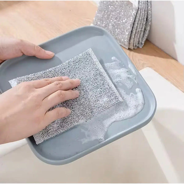 Hand scrubbing a gray dish with foamy gray cleaning pad and stacked double sided scrubber pads