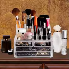 Clear makeup organizer with drawers holding brushes lipsticks and skincare bottles on wooden surface