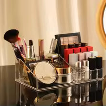 Clear makeup organizer with drawers holding brushes, lipsticks, and cosmetics on a vanity table