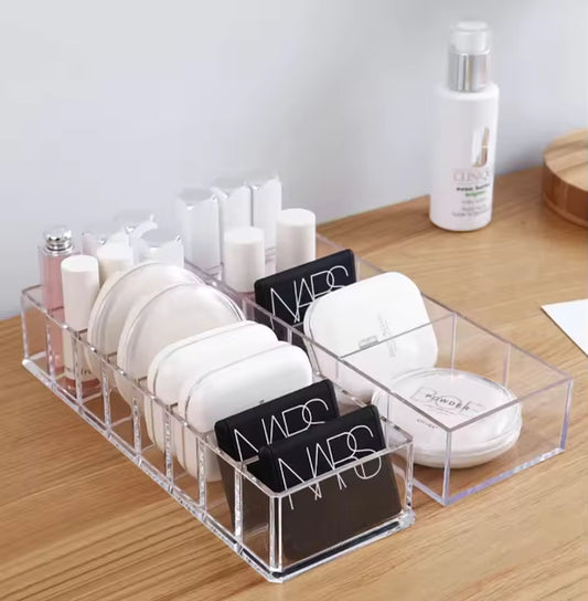 Clear 8 compartment organizer holding makeup compacts and bottles on wooden surface