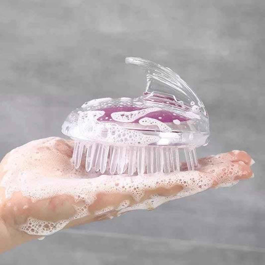 Clear silicone scalp massage brush with soft bristles held in a soapy hand for hair cleaning