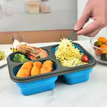 Blue collapsible silicone lunch box with four compartments holding noodles, shrimp, broccoli, and orange slices