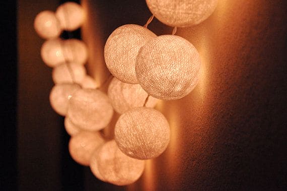 Warm white lit cotton ball string lights hanging against a dark wall creating cozy ambient lighting