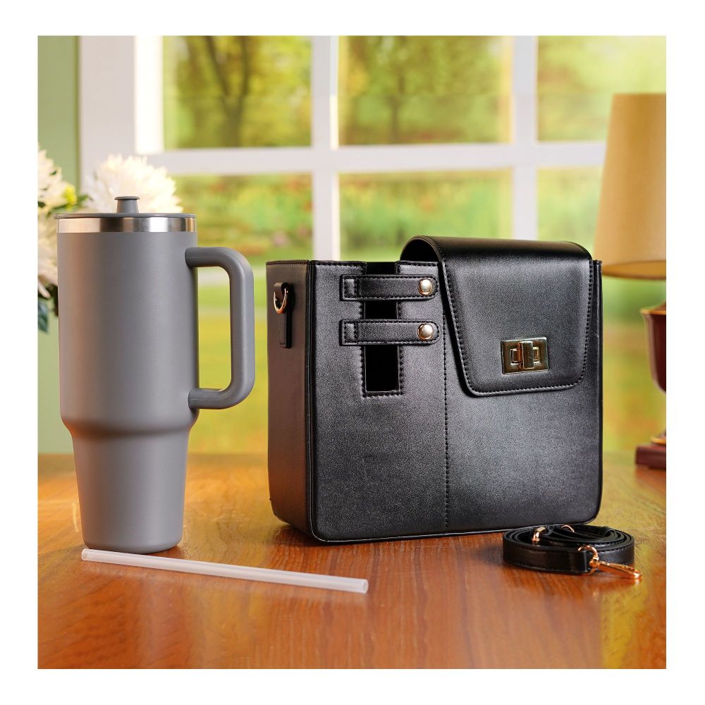 Black crossbody water bottle carrier bag with adjustable strap and secure clasp on wooden table next to gray travel mug