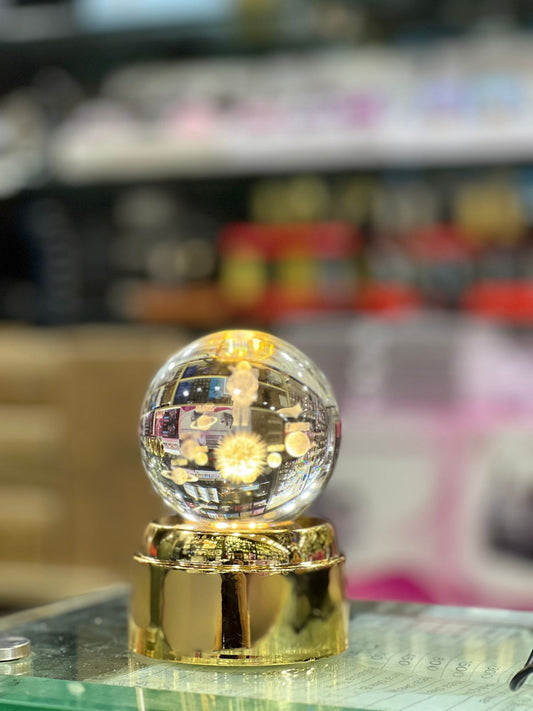 Clear crystal ball lamp with golden base glowing on glass surface in indoor setting