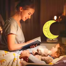 Crystal moon night light lamp glowing softly next to child sleeping with woman reading a book