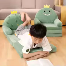 Cute cartoon children sofa shaped like green dinosaurs with crowns in living room with child reading book