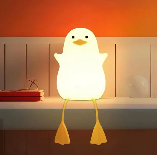 Cute duck night lamp glowing softly with yellow feet sitting on a white shelf by Clarify.pk