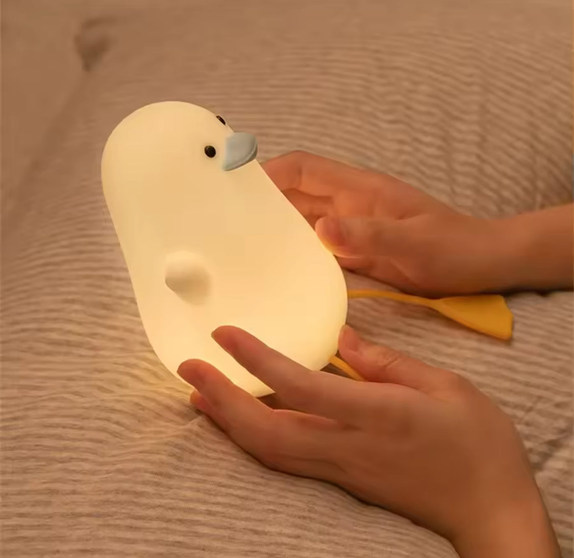 Hands holding a glowing cute duck night lamp with soft light on a textured surface