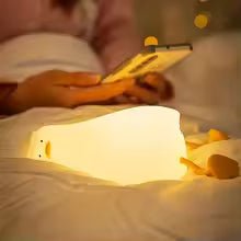 Clarify.pk cute duck night light glowing softly on a bed beside a person using a smartphone