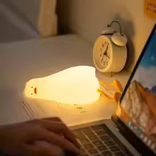 Cute duck night light glowing softly on desk beside laptop and alarm clock