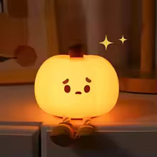 Cute silicone pumpkin night light glowing softly with a sad face on a bedside table