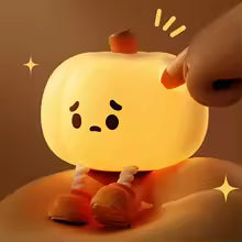 Cute silicone pumpkin night light glowing warmly with a small hand pressing the top