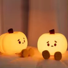 Cute silicone pumpkin night light with adorable face designs glowing warmly on a soft surface