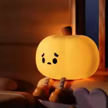 Cute silicone pumpkin night light with a sad face sitting on a surface near a window at night