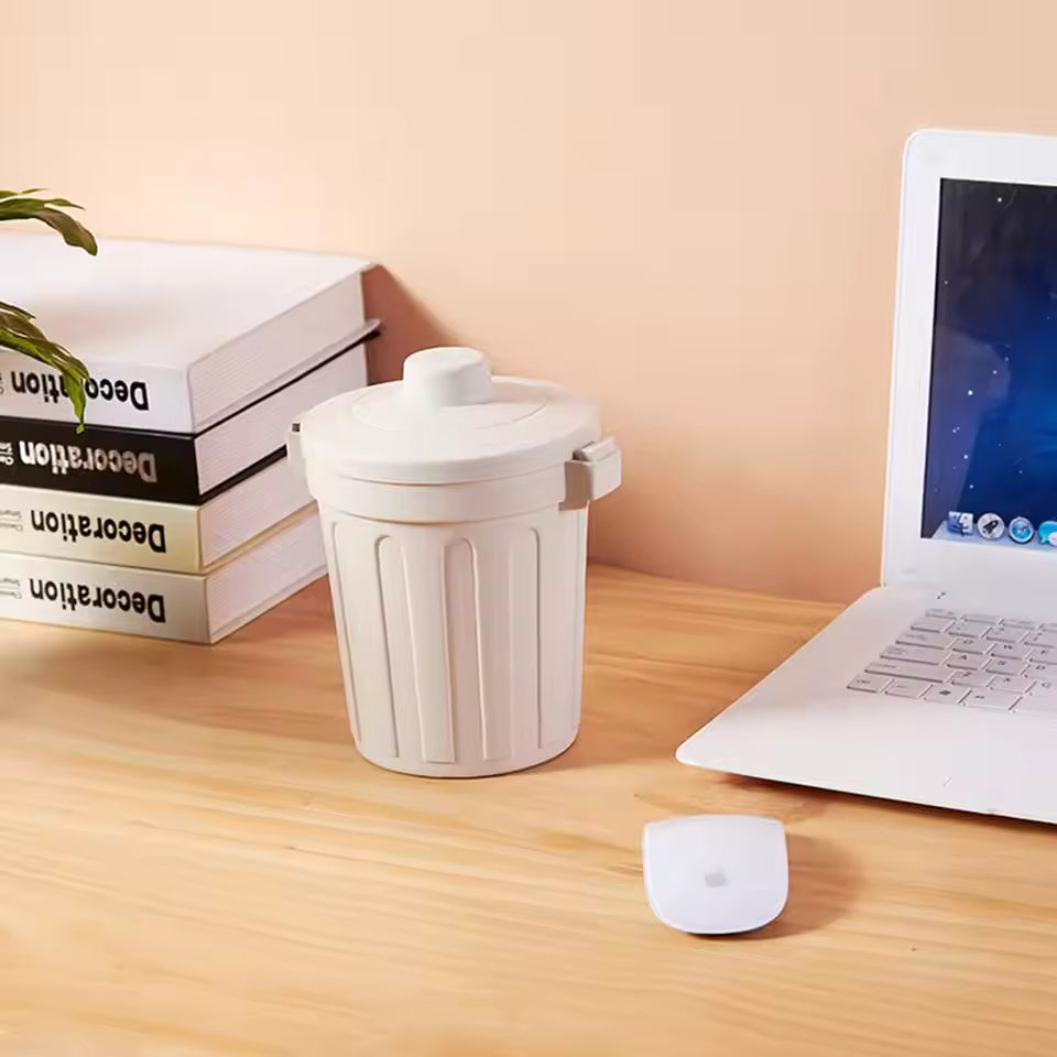 White desktop mini trash can placed on wooden desk next to laptop and stacked books