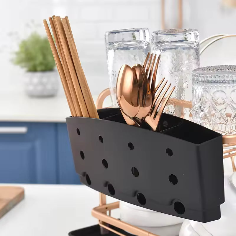 Black dish drying rack with cutlery holder containing gold utensils and wooden chopsticks on a kitchen counter