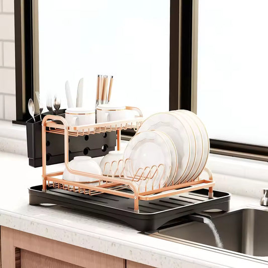Rose gold dish drying rack with cutlery holder and black tray on kitchen counter near window