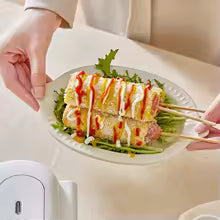 Double sided sandwich press used to prepare grilled sandwiches served on a plate with sauce and greens