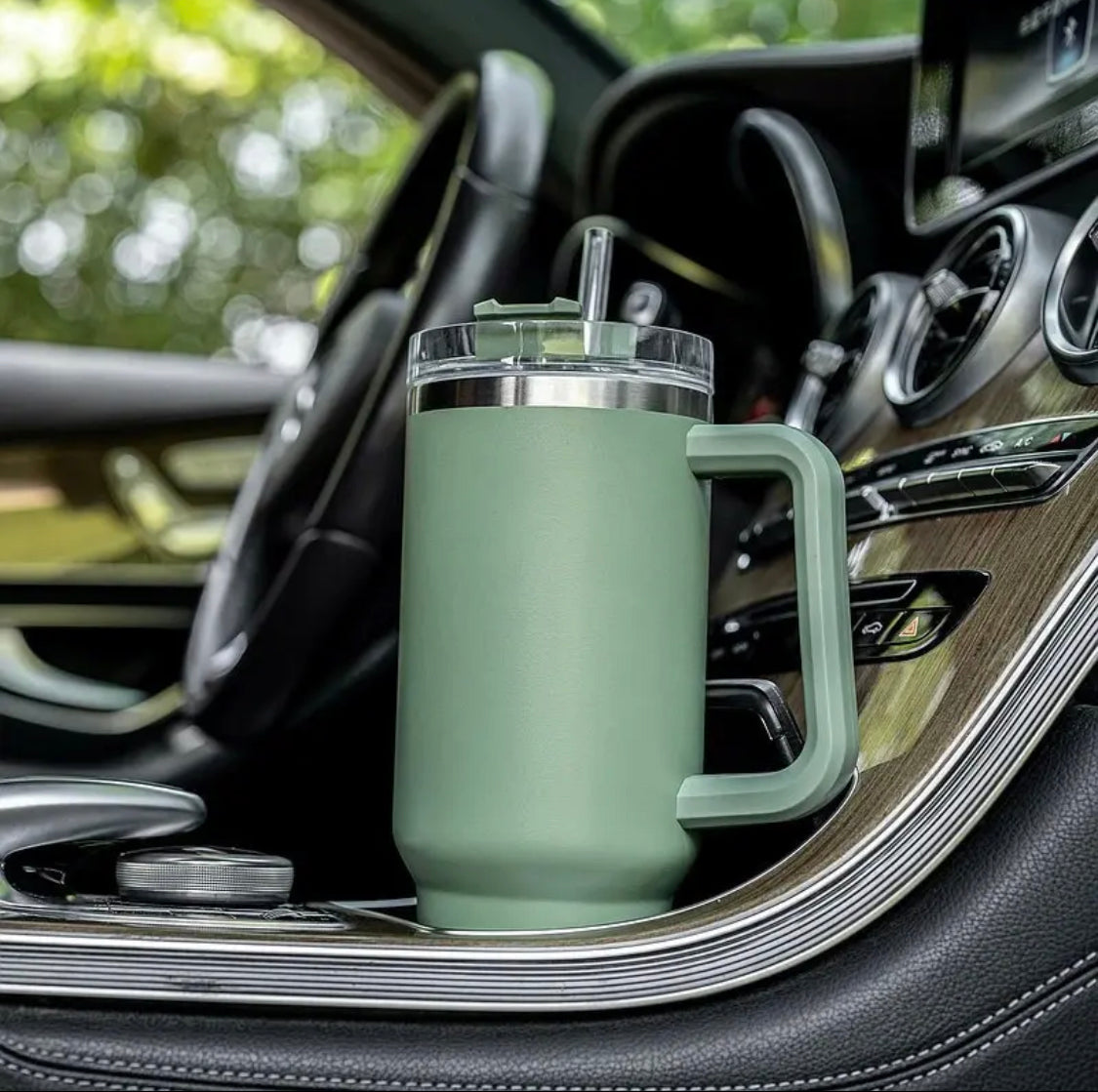 Green double wall vacuum tumbler with handle and clear lid placed in car cup holder