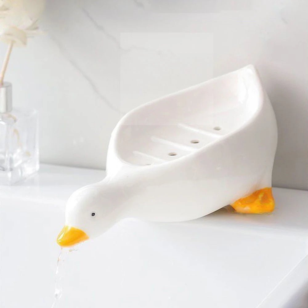 White duck-shaped soap dish with yellow beak and feet holding soap on bathroom sink