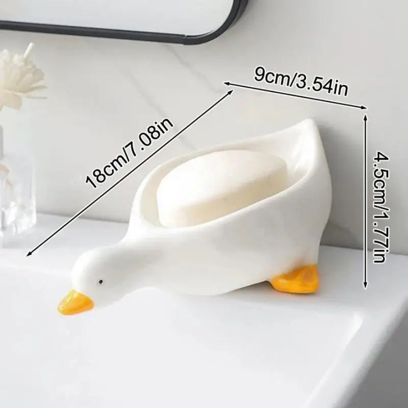 Duck-shaped soap dish by Clarify.pk in white with yellow beak and feet holding a soap bar