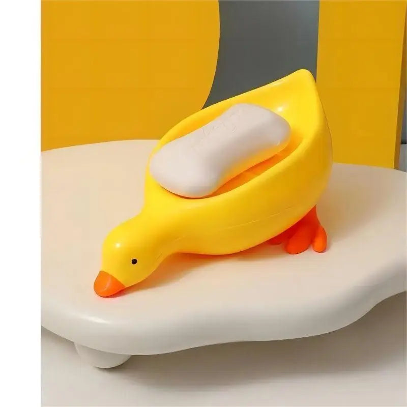 Yellow duck-shaped soap dish with orange beak and feet holding a white soap bar
