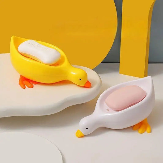 Clarify.pk duck-shaped soap dish in yellow and white holding bars of soap on white surface