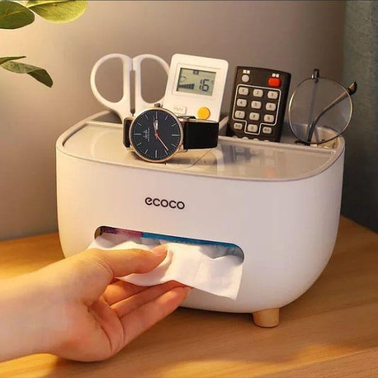White Ecoco tissue box holder with storage compartments holding scissors, watch, remote, and glasses on a wooden surface