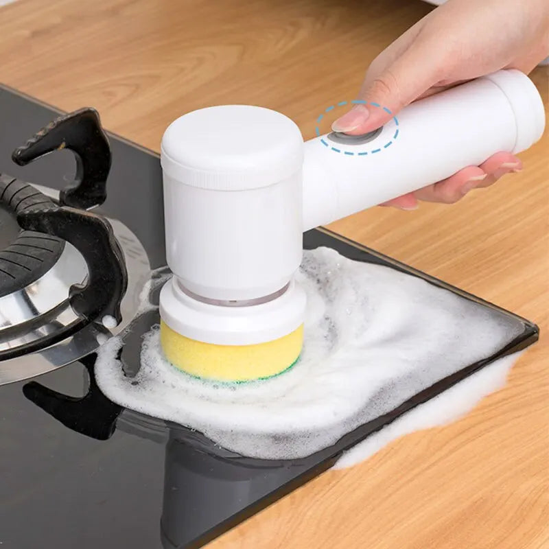 Hand holding white electric cleaning brush scrubbing stove top with foam for household cleaning