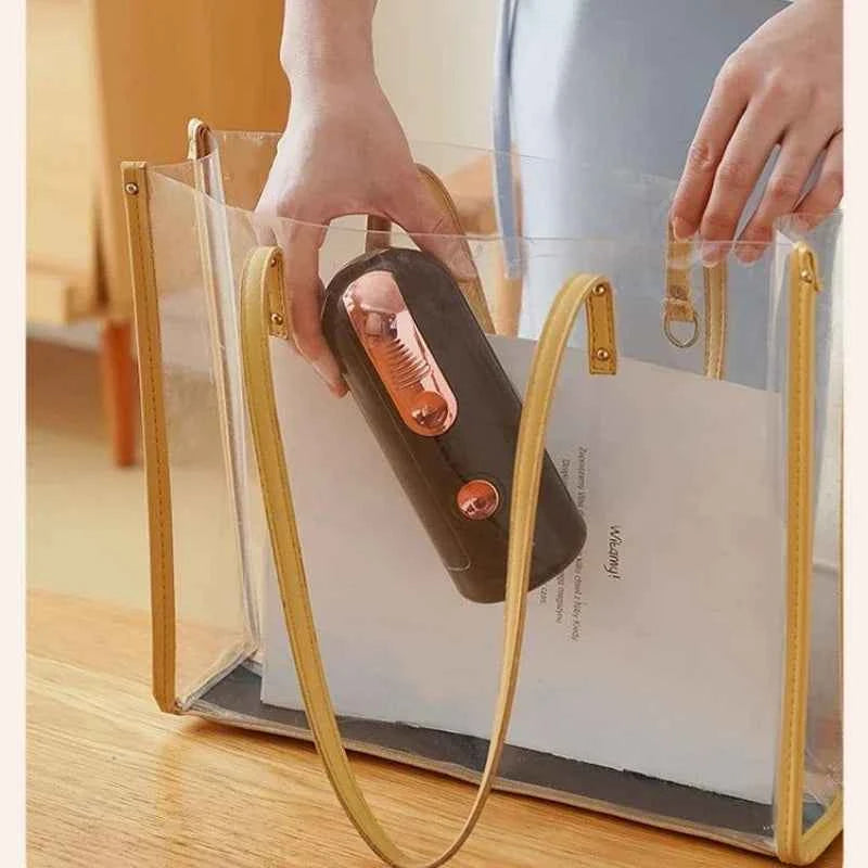 Portable electric water bottle pump in black being placed inside a clear tote bag
