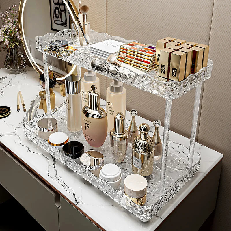 Clear two-tier bathroom organizer shelves holding skincare and makeup products on marble countertop