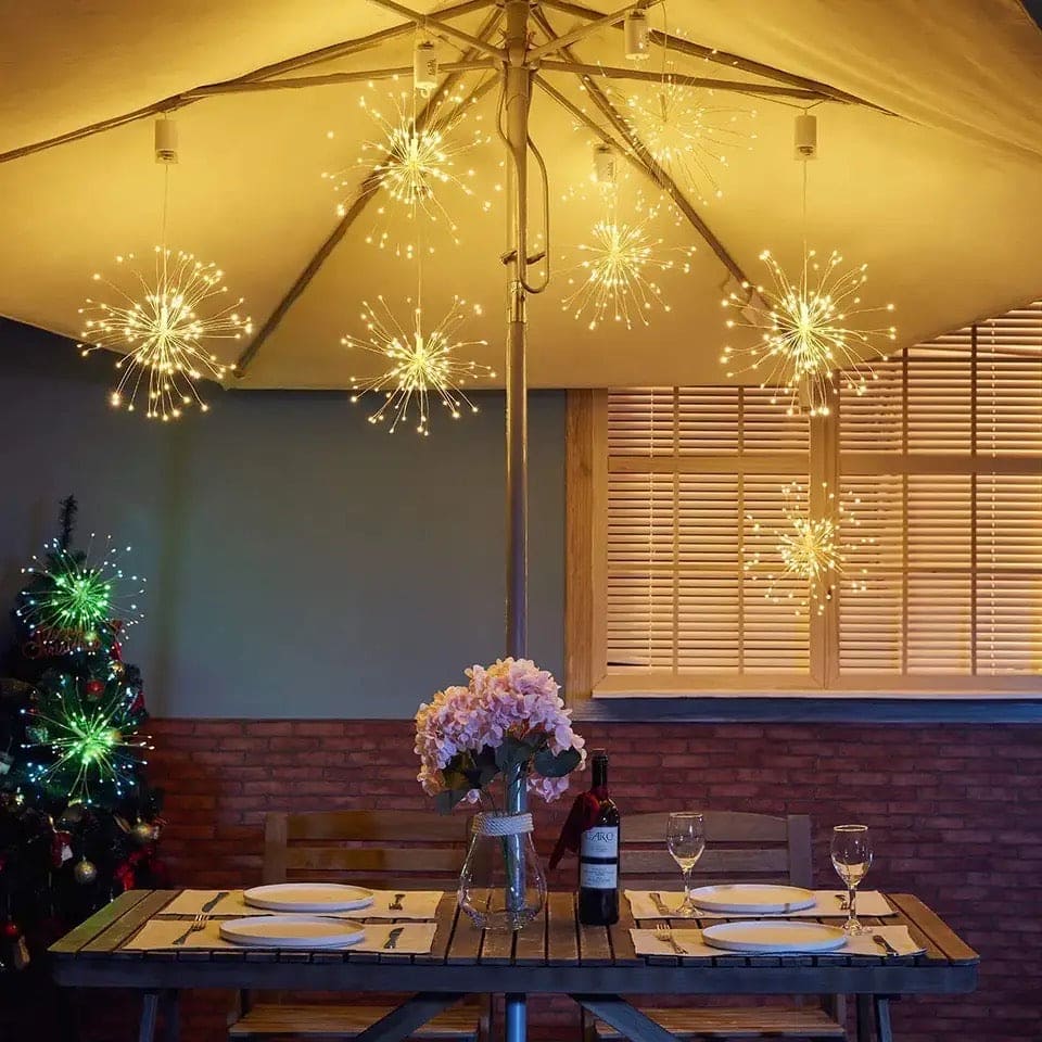 Firework string lights battery operated hanging from outdoor umbrella over dining table with flowers and wine bottle
