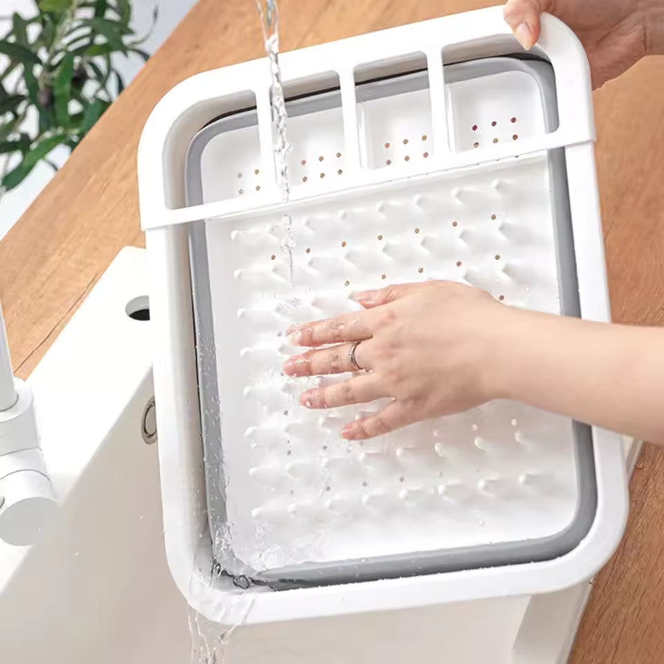 White foldable dish drainer rack being rinsed with water in a kitchen sink