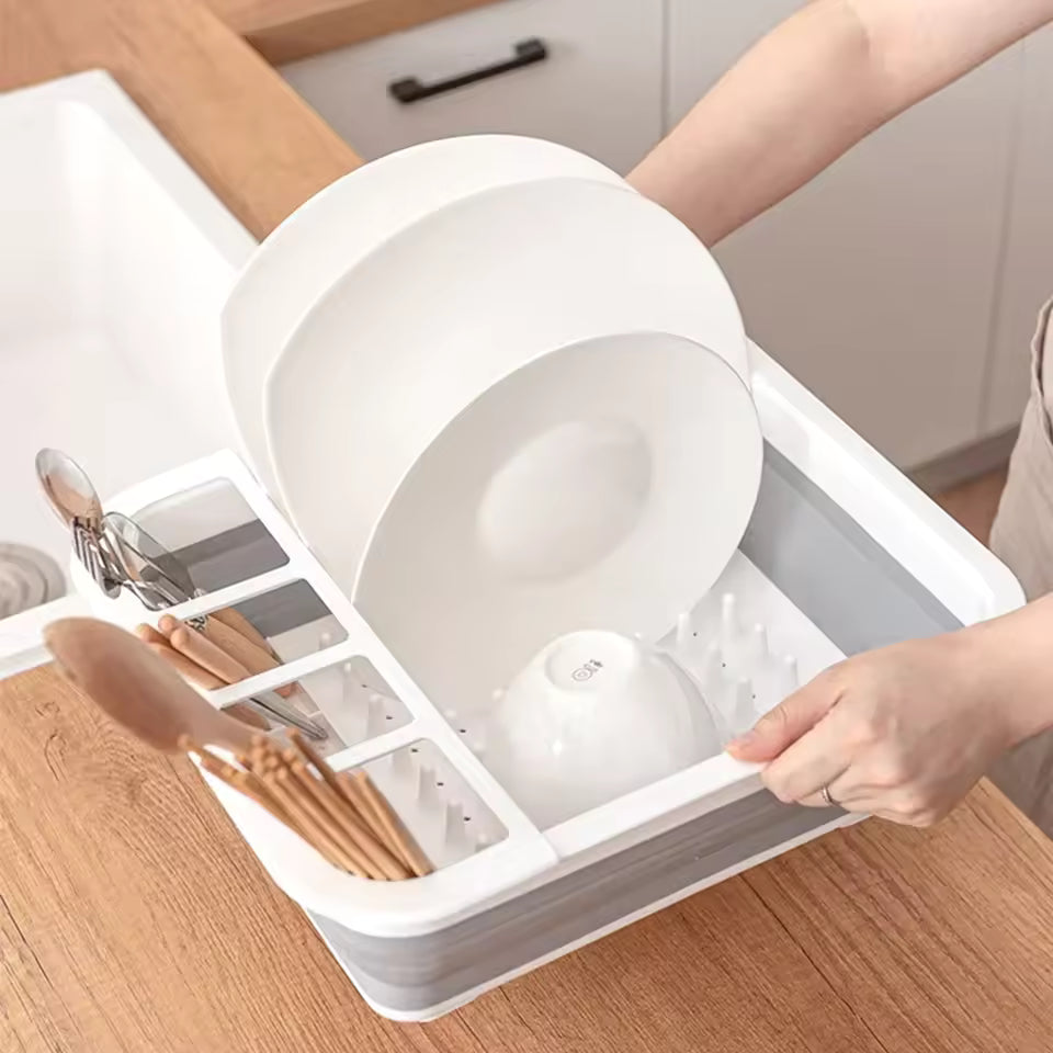 White foldable dish drainer rack with compartments holding plates, bowls, and utensils on kitchen counter