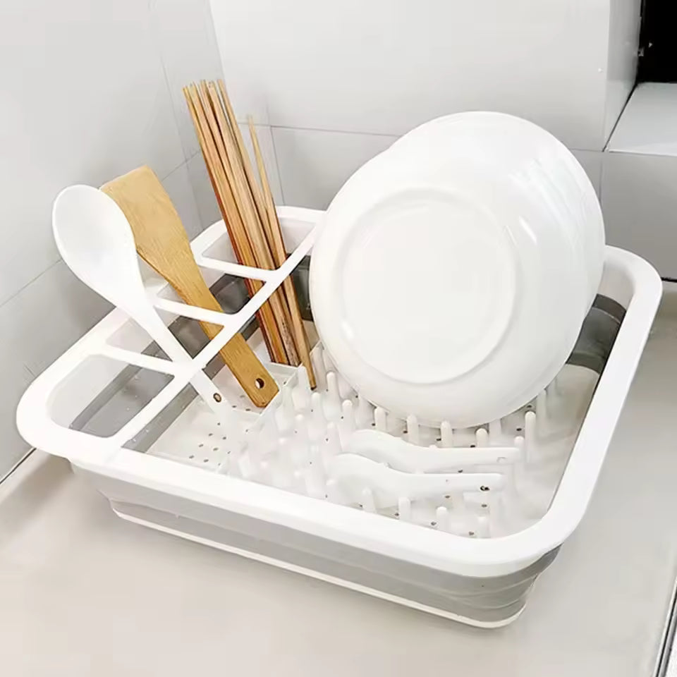 White foldable dish drainer rack holding plates, wooden utensils, and chopsticks on kitchen counter