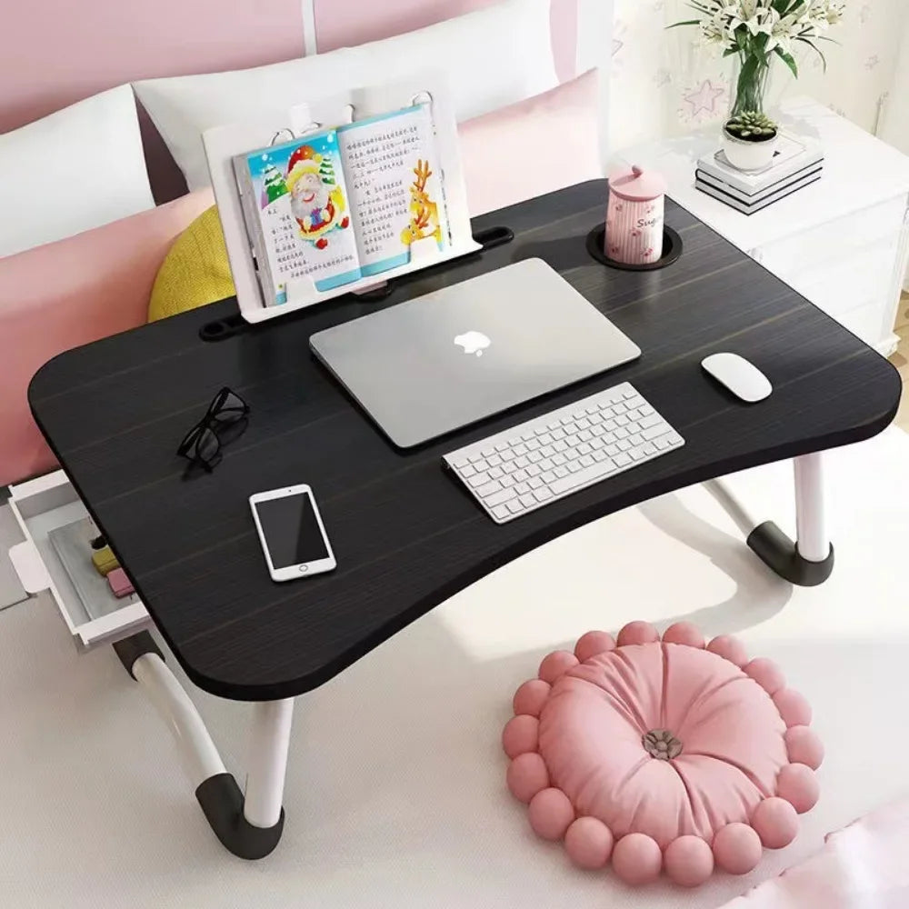 Black foldable laptop desk with white legs holding a laptop keyboard mouse phone glasses and book stand
