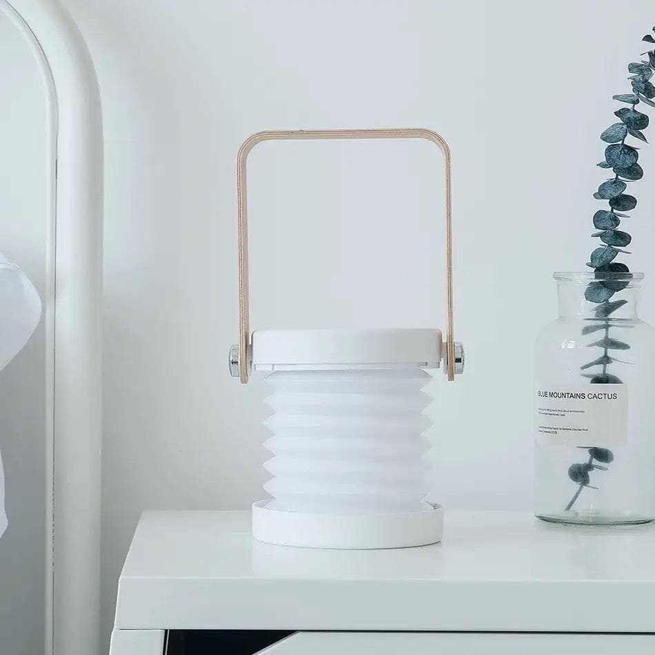 Minimalist white foldable LED table lamp with wooden handle placed on a white bedside table